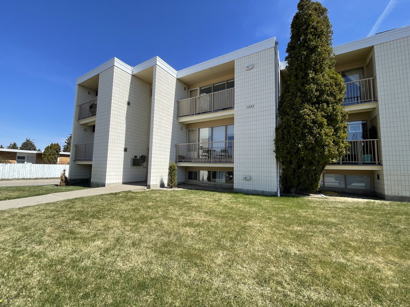 Exterior of the apartment building at 1327 Scenic Drive S, with balconies, lawn and a clear blue sky